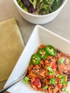 Bowl of Vegan Black Bean Jambalaya topped with Jalapeno peppers and parsley. Side salad and a fork in the bowl.